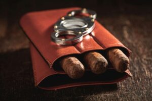 Three cigars in a leather container with a cutter